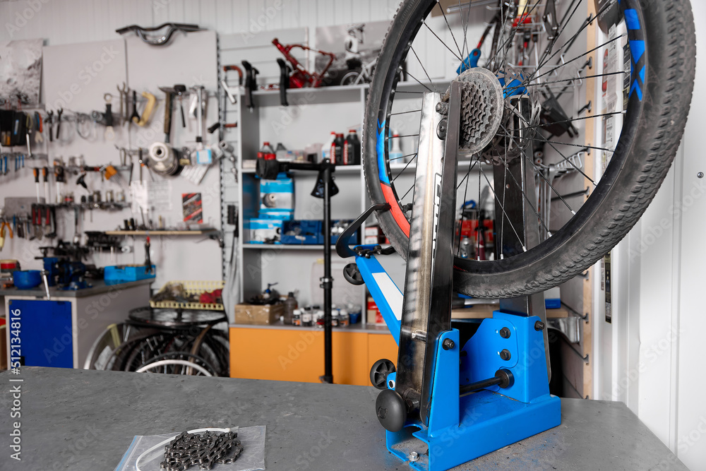 Bicycle wheel holder stand is placed on a table for repairing bicycle equipment in the workshop. Against the background of the wall with tools close-up is a blue bicycle wheel holder. Bicycle service