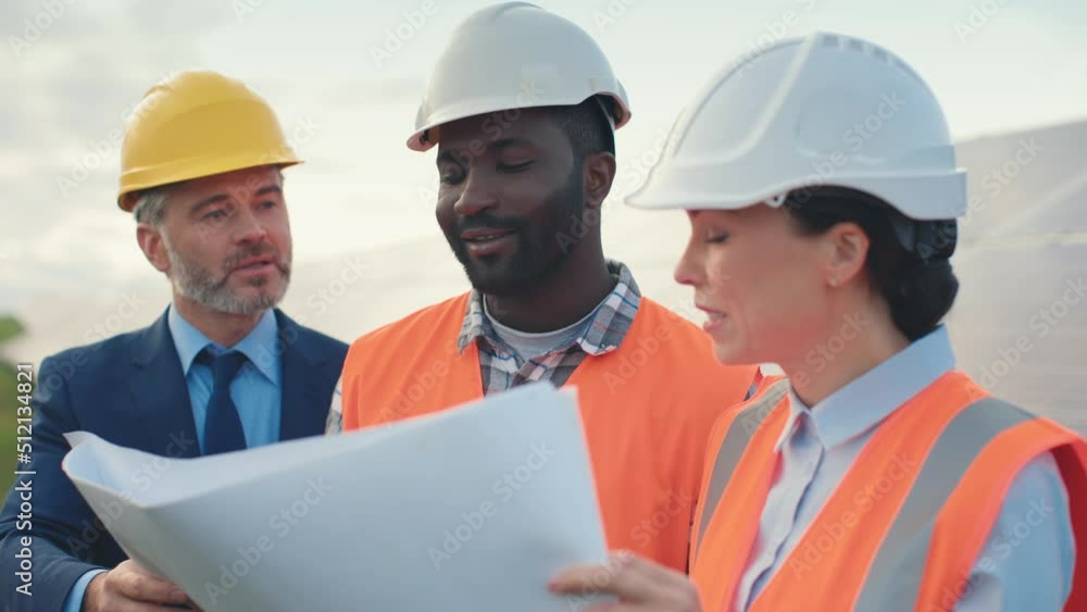 Close-up of employees of modern solar panel station in hard hats standing outside and studying new paper plan with project manager. Close-up of employees of modern solar panel station in hard hats standing outside and studying new paper plan with project manager.