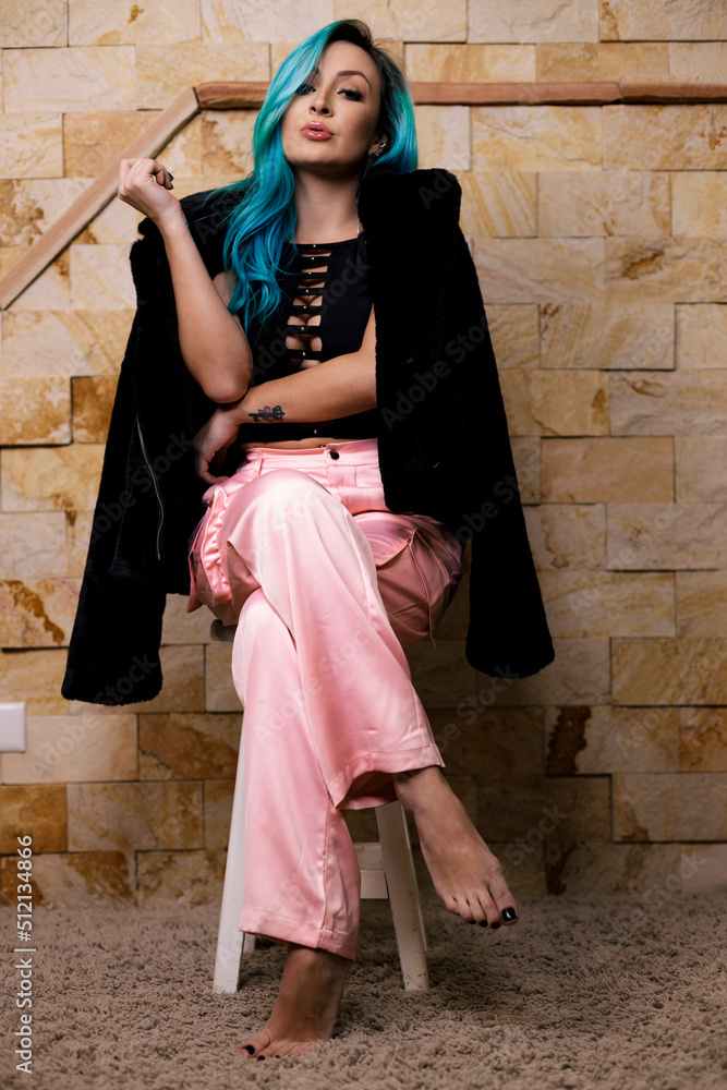 Beautiful blue hair fancy elegant woman in black jacket and white pants sitting on a bench looking confident and sensual and powerful
