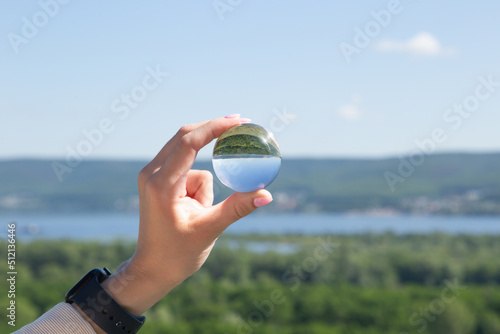 A look at the upside-down world through a ball. The girl's hand holds a crystal ball in which the image of mountains is inverted. Focus on the crystal ball. Take care of nature. Close-up