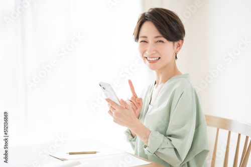 リビングで椅子に座りながら携帯電話を持っている笑顔の日本人女性