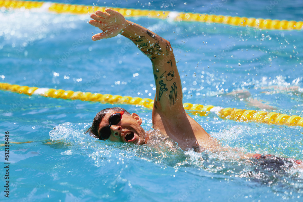 Young muscular man, professional swimmer in goggles training at public swimming-pool, outdoors. Sport, power, energy, style, hobby concept.