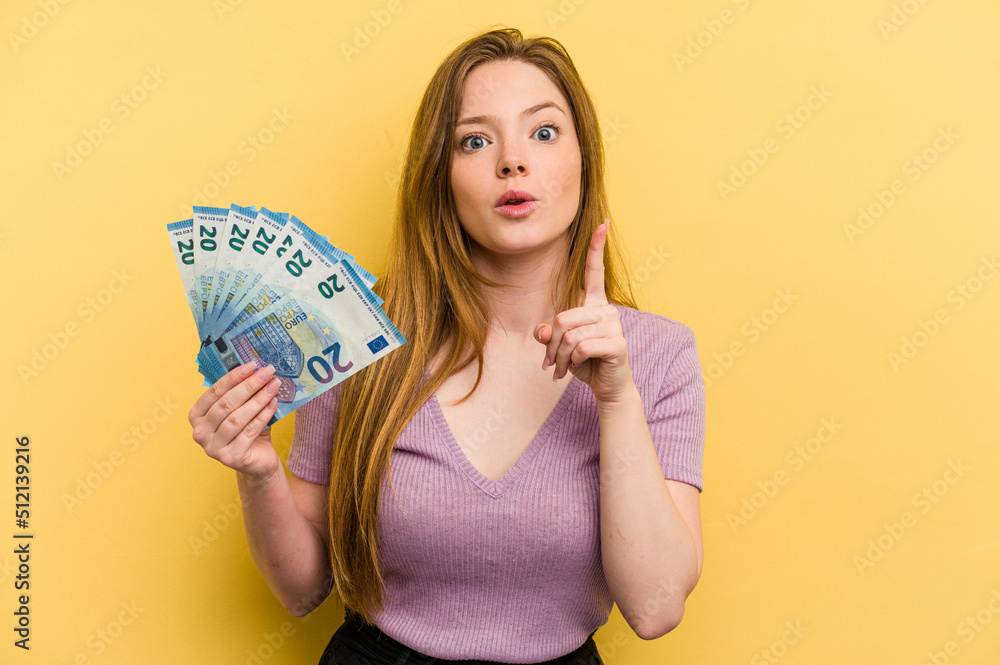 Young caucasian woman holding banknotes isolated on yellow background having an idea, inspiration concept. Young caucasian woman holding banknotes isolated on yellow background having an idea, inspiration concept.