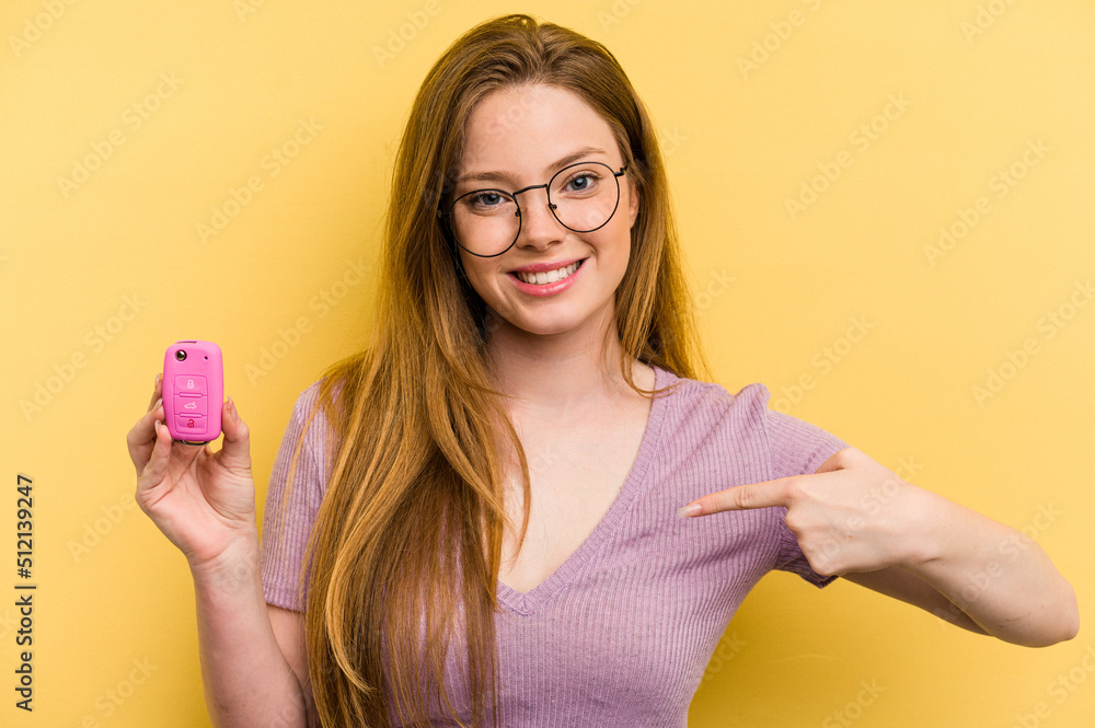 Young caucasian woman holding car keys isolated on yellow background person pointing by hand to a shirt copy space, proud and confident Young caucasian woman holding car keys isolated on yellow background person pointing by hand to a shirt copy space, proud and confident