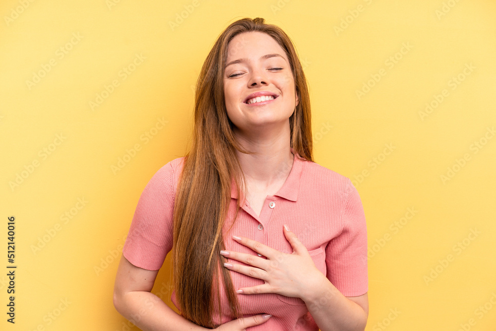 Fototapeta premium Young caucasian woman isolated on yellow background laughs happily and has fun keeping hands on stomach.