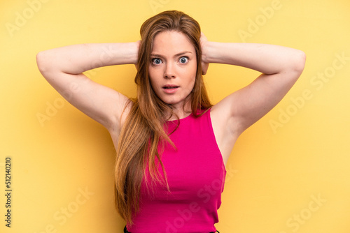 Young caucasian woman isolated on yellow background covering ears with hands trying not to hear too loud sound. © Asier