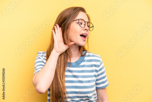 Young caucasian woman isolated on yellow background trying to listening a gossip.