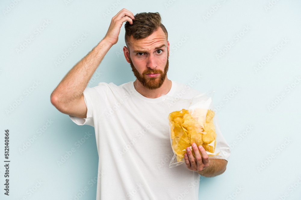 Young caucasian man holding crisps isolated on blue background being shocked, she has remembered important meeting.