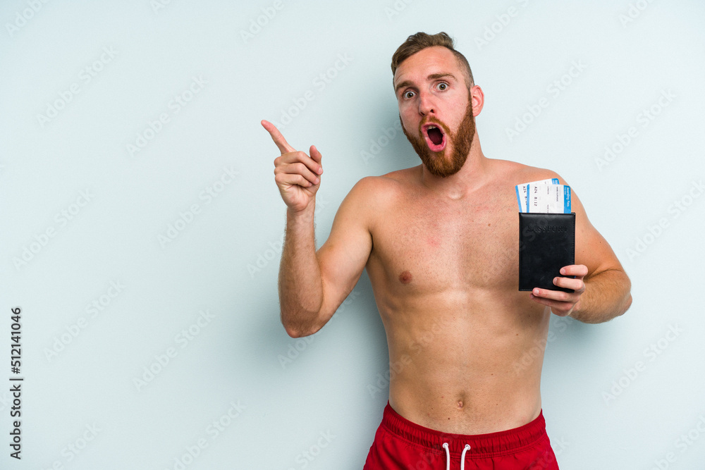 Fototapeta premium Young caucasian man holding a passport isolated on blue background pointing to the side