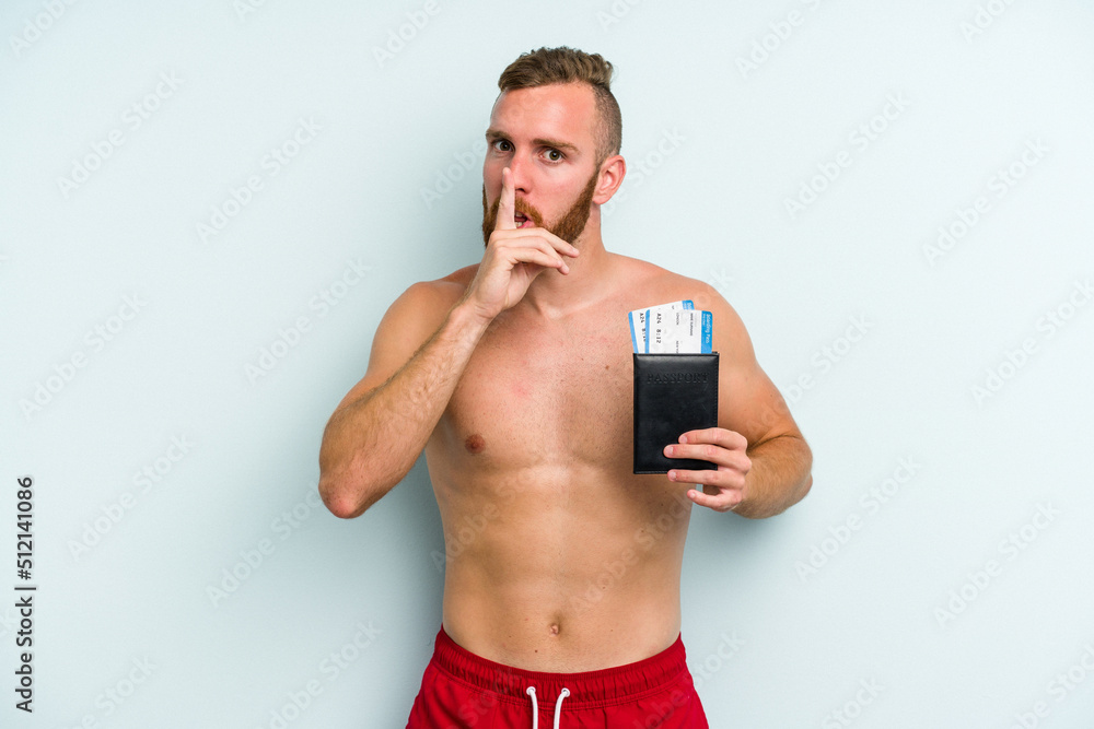 Fototapeta premium Young caucasian man holding a passport isolated on blue background keeping a secret or asking for silence.