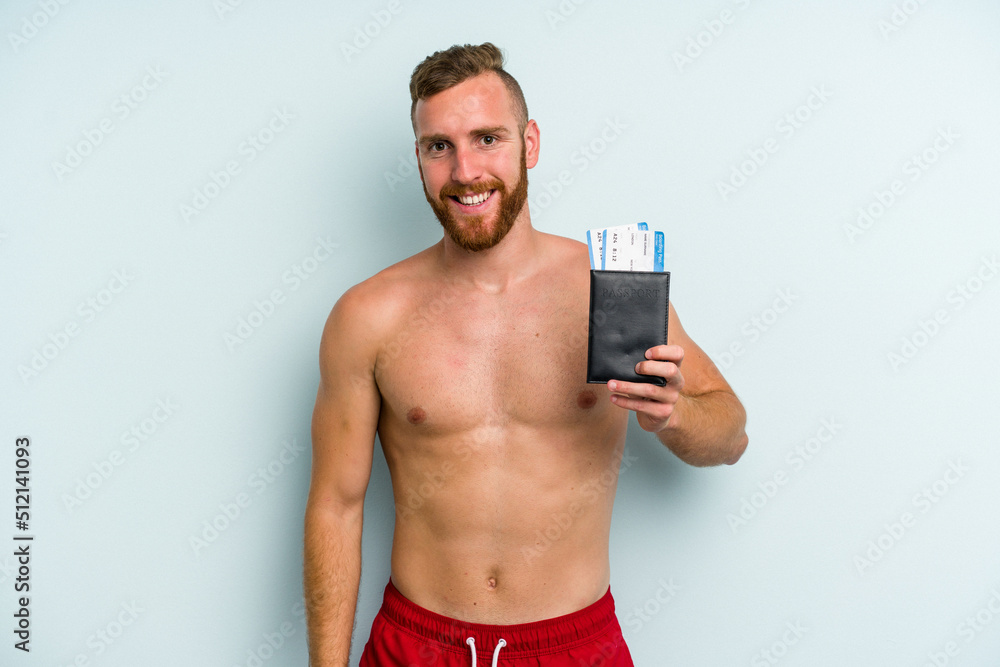 Fototapeta premium Young caucasian man holding a passport isolated on blue background happy, smiling and cheerful.