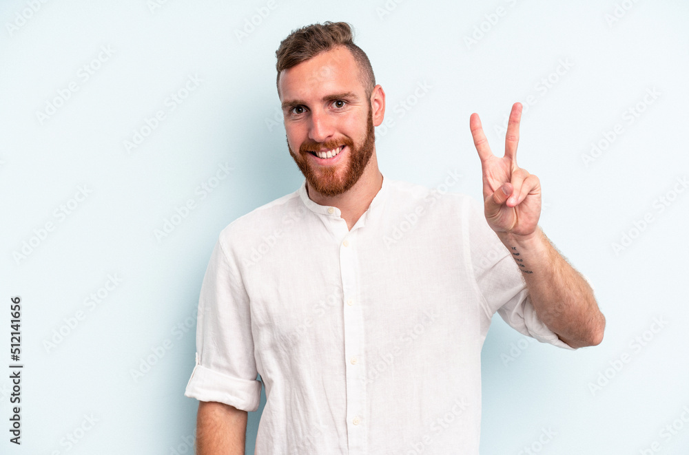 Young caucasian man isolated on blue background showing victory sign and smiling broadly. Young caucasian man isolated on blue background showing victory sign and smiling broadly.