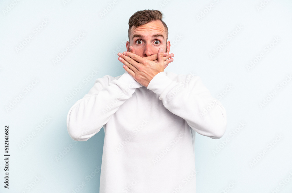 Young caucasian man isolated on blue background shocked covering mouth with hands. Young caucasian man isolated on blue background shocked covering mouth with hands.