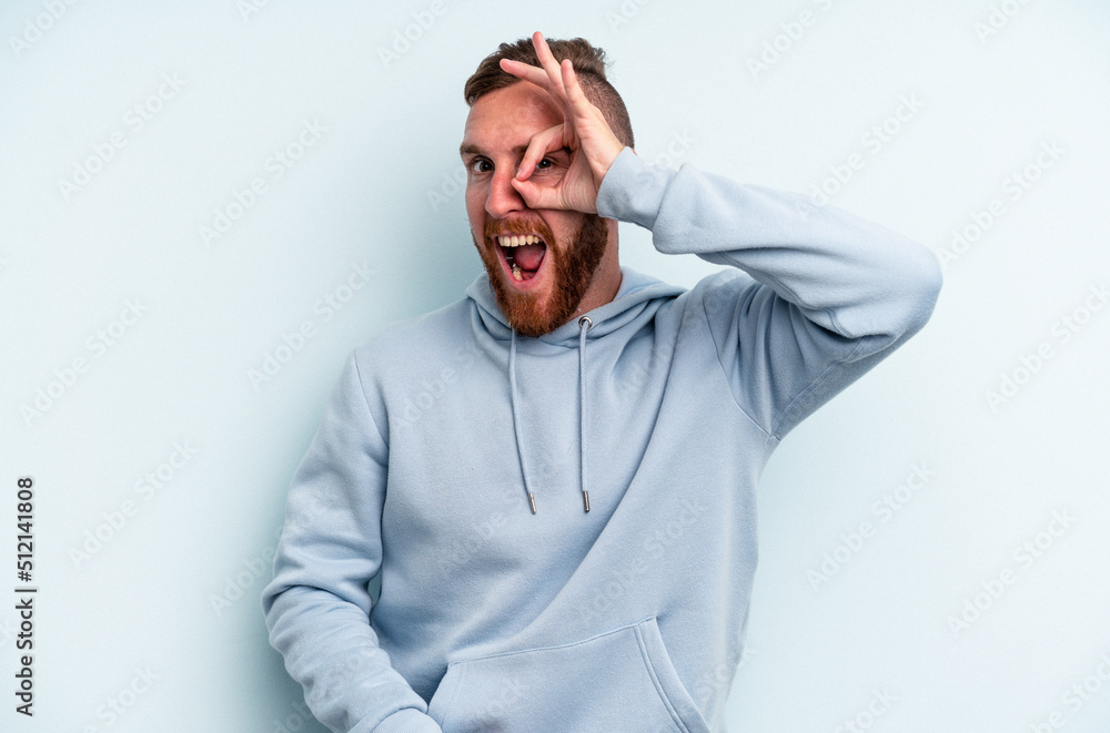 Young caucasian man isolated on blue background excited keeping ok gesture on eye. Young caucasian man isolated on blue background excited keeping ok gesture on eye.