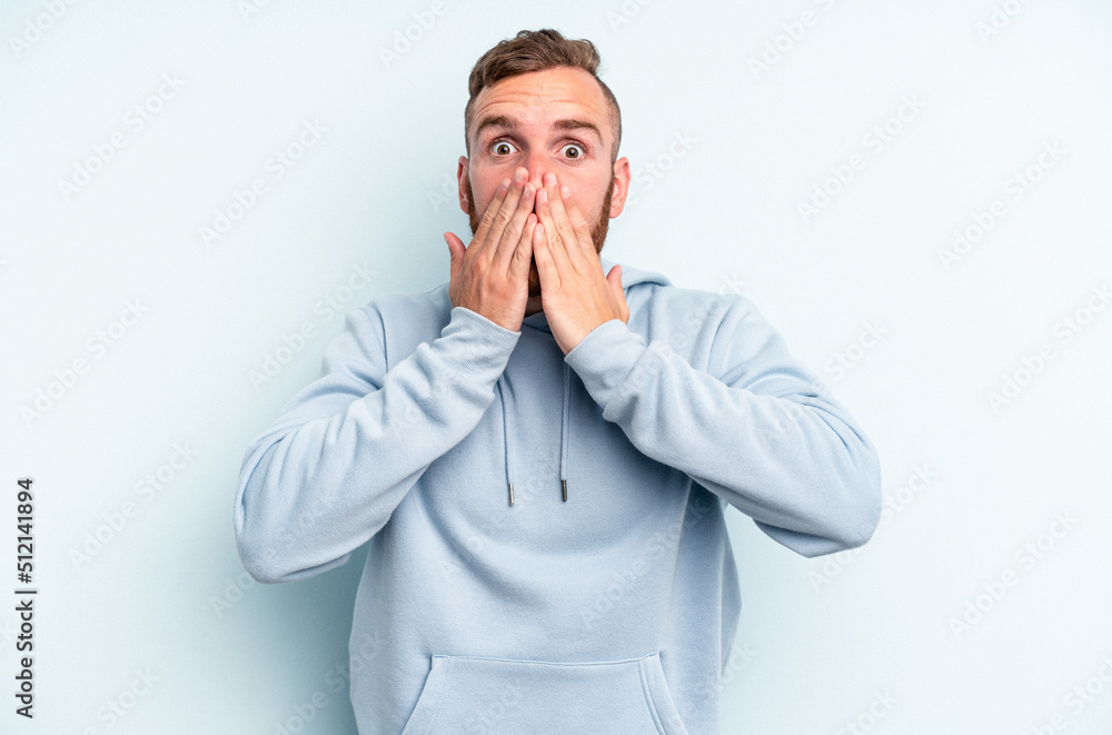 Young caucasian man isolated on blue background shocked covering mouth with hands. Young caucasian man isolated on blue background shocked covering mouth with hands.