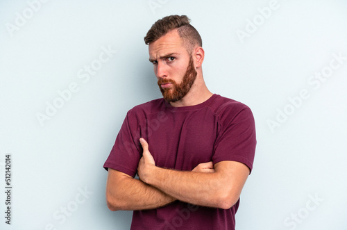 Fototapeta Young caucasian man isolated on blue background frowning face in displeasure, keeps arms folded