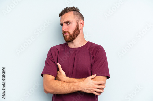 Young caucasian man isolated on blue background suspicious, uncertain, examining you.