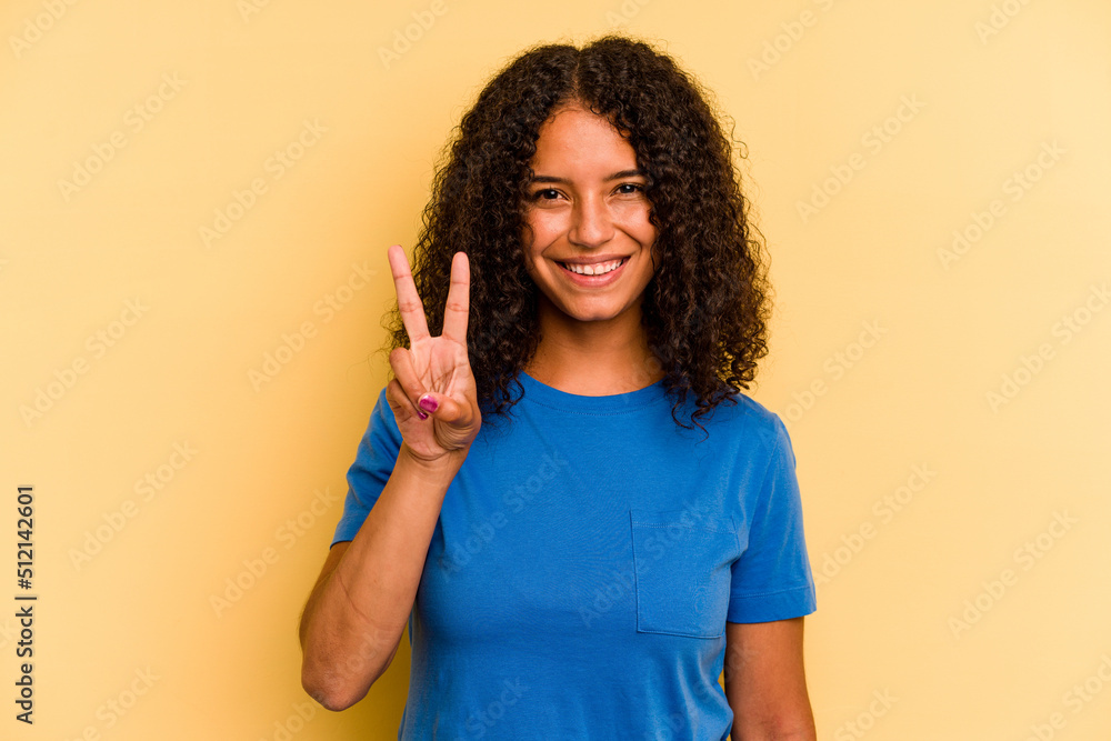 Young Brazilian woman isolated on yellow background showing victory sign and smiling broadly. Young Brazilian woman isolated on yellow background showing victory sign and smiling broadly.