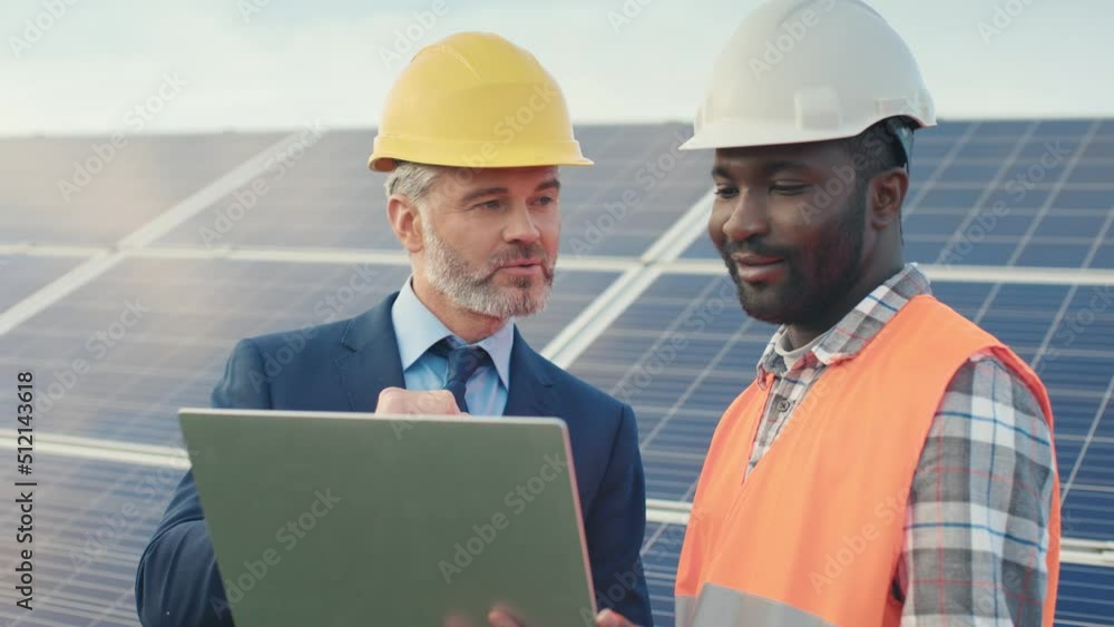 Close up of caucasian businessman and african american worker standing on street against sunny background and discussing work tasks while browsing list on laptop. Close up of caucasian businessman and african american worker standing on street against sunny background and discussing work tasks while browsing list on laptop.