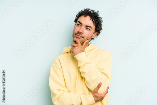 Young caucasian man isolated on blue background thinking and looking up, being reflective, contemplating, having a fantasy.