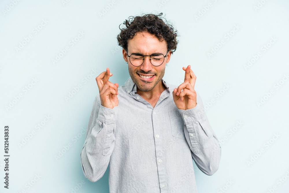 Young caucasian man isolated on blue background crossing fingers for having luck Young caucasian man isolated on blue background crossing fingers for having luck