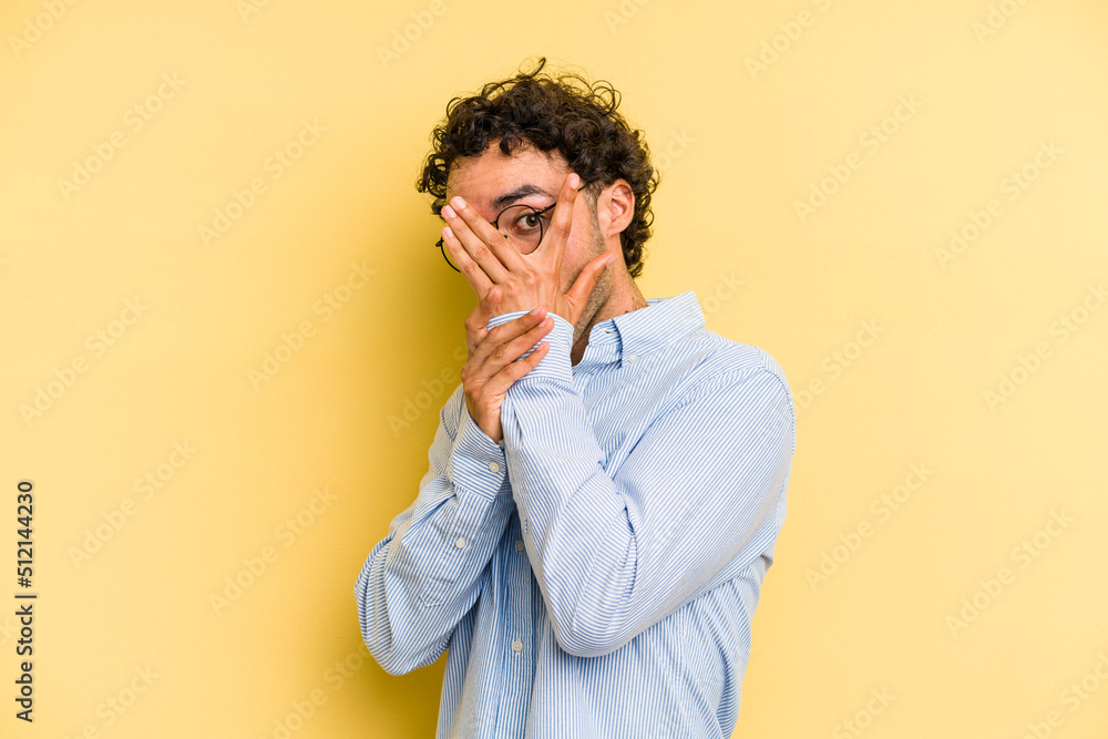 Young caucasian man isolated on yellow background blink through fingers frightened and nervous. Young caucasian man isolated on yellow background blink through fingers frightened and nervous.