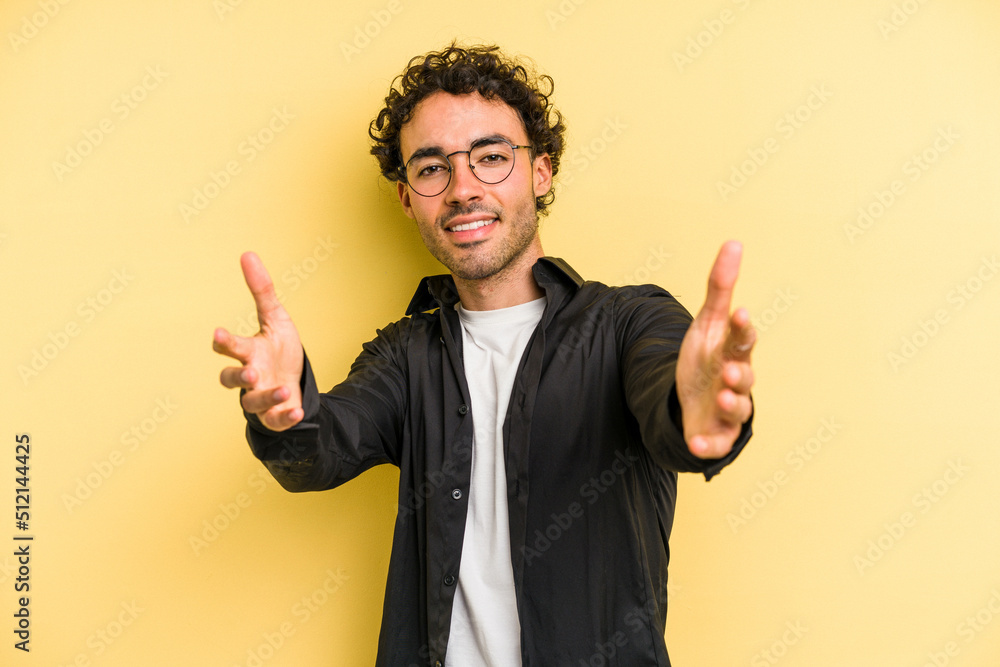 Young caucasian man isolated on yellow background feels confident giving a hug to the camera. Young caucasian man isolated on yellow background feels confident giving a hug to the camera.