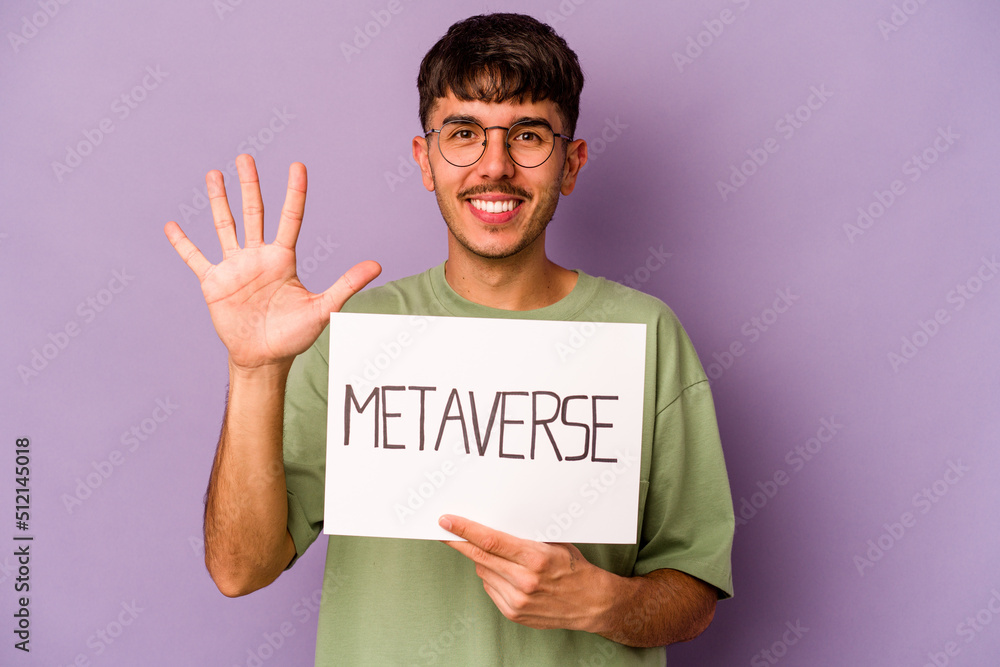 Young hispanic man holding meta verse placard isolated on purple background smiling cheerful showing number five with fingers. Young hispanic man holding meta verse placard isolated on purple background smiling cheerful showing number five with fingers.