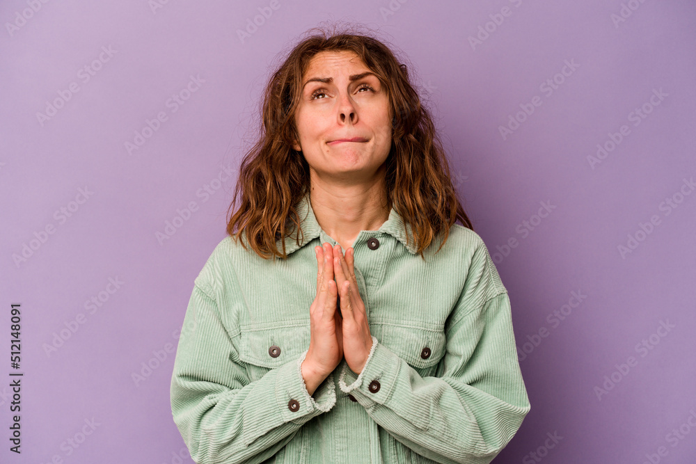 Young caucasian woman isolated on purple background holding hands in pray near mouth, feels confident. Young caucasian woman isolated on purple background holding hands in pray near mouth, feels confident.