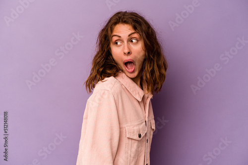 Young caucasian woman isolated on purple background looks aside smiling, cheerful and pleasant.