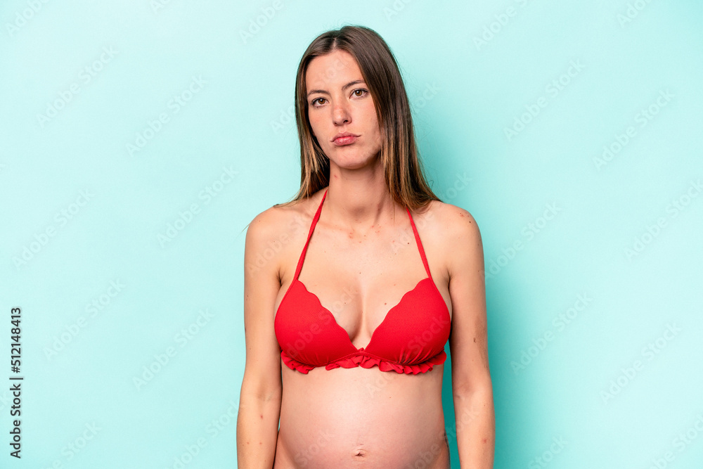Young caucasian pregnant woman wearing bikini isolated on blue background confused, feels doubtful and unsure. Young caucasian pregnant woman wearing bikini isolated on blue background confused, feels doubtful and unsure.