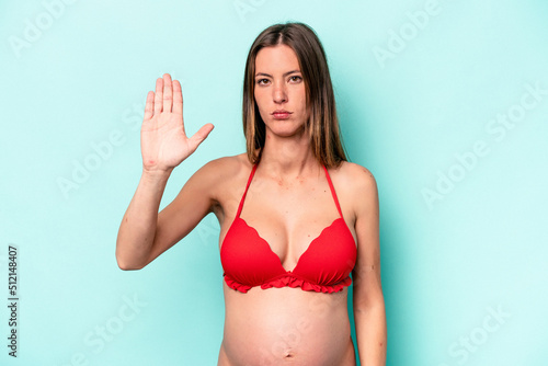 Young caucasian pregnant woman wearing bikini isolated on blue background standing with outstretched hand showing stop sign, preventing you.