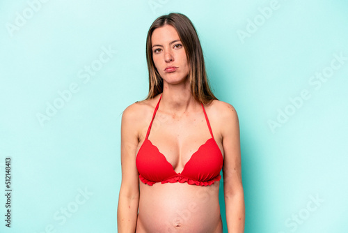 Young caucasian pregnant woman wearing bikini isolated on blue background confused, feels doubtful and unsure. © Asier