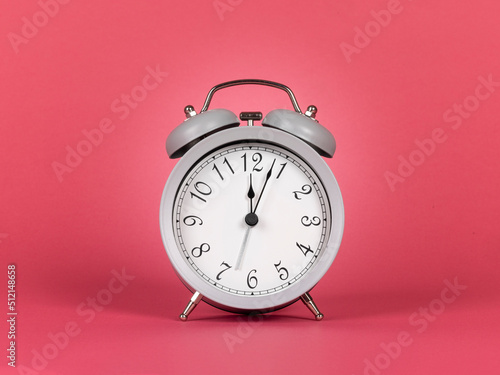 Grey alarmclock with bells, showing twelf as time. Isolated on a watermelon pink background.