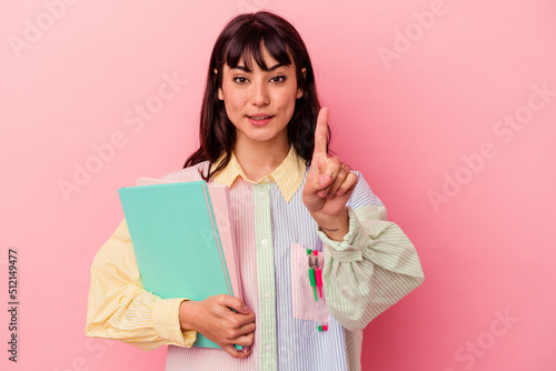 Young student caucasian woman holding books isolated on pink background showing number one with finger.