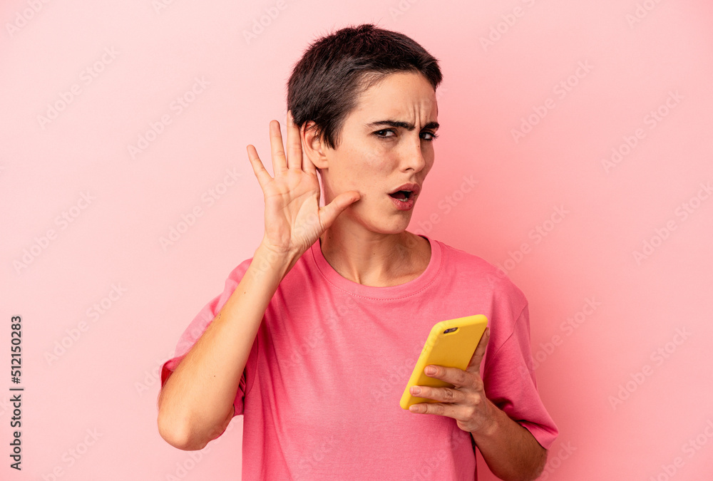 Young caucasian woman holding mobile phone isolated on pink background trying to listening a gossip. Young caucasian woman holding mobile phone isolated on pink background trying to listening a gossip.