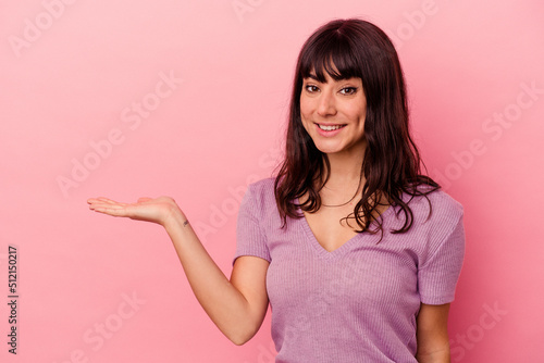 Young caucasian woman isolated on pink background showing a copy space on a palm and holding another hand on waist. © Asier