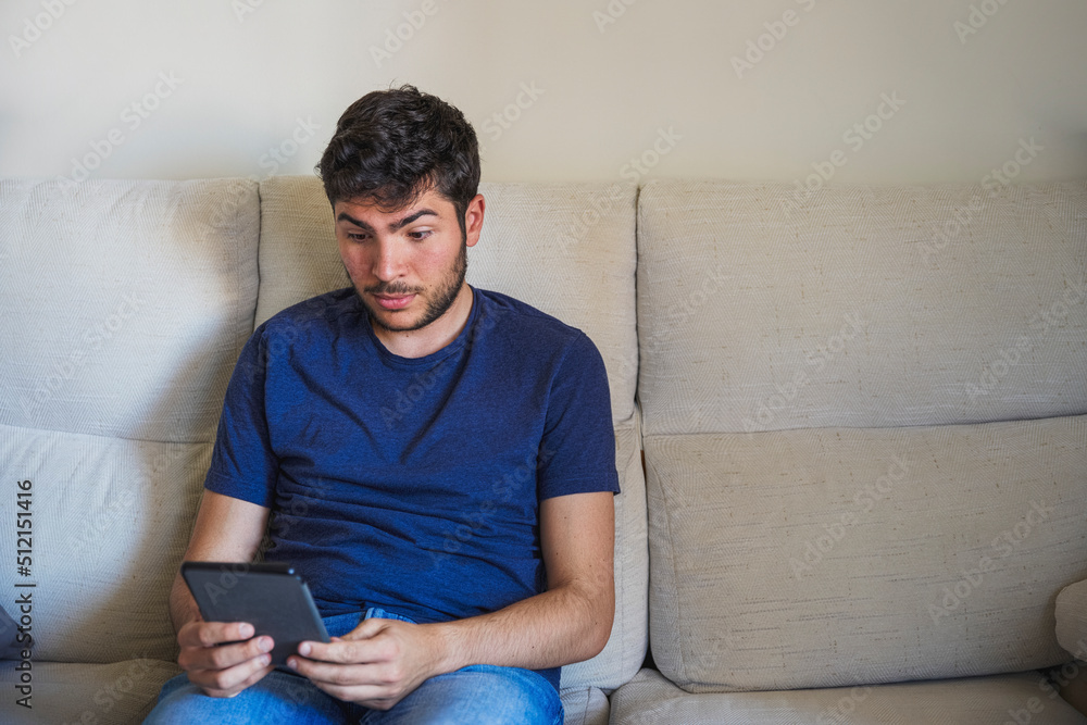 Young man surprised reading with his ebook on a sofa Young man surprised reading with his ebook on a sofa