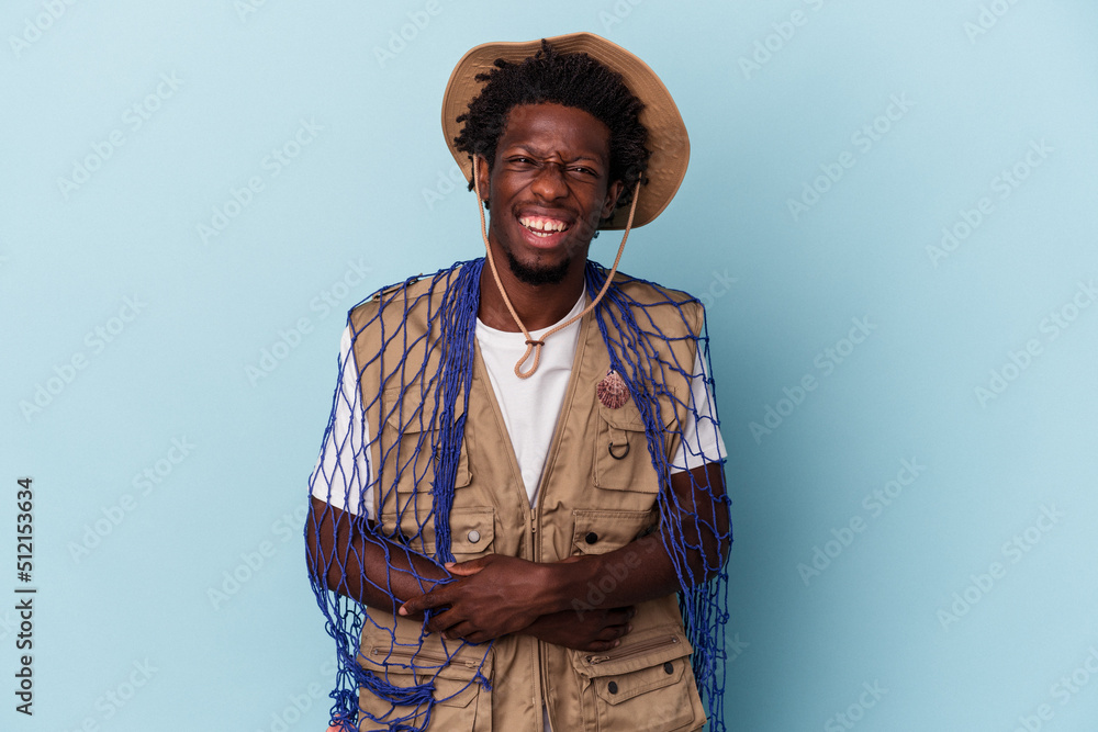 Young african american fisherman holding a net isolated on blue background laughing and having fun. Young african american fisherman holding a net isolated on blue background laughing and having fun.