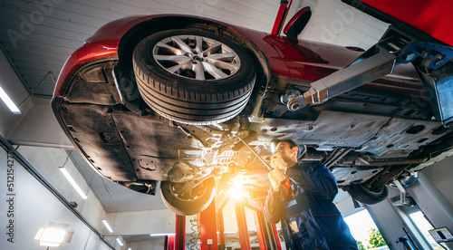 Принти на полотні Young car mechanic at repair service station inspecting car wheel and suspension detail of lifted automobile