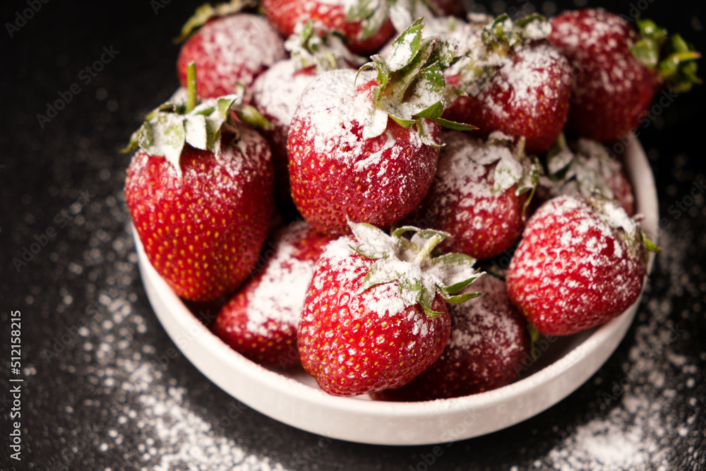 Strawberries in a plate with powdered sugar on a black background, close-up. Strawberries in a plate with powdered sugar on a black background, close-up.