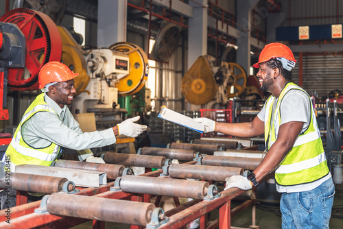 African American worker man are handing industrial machinery maintenance report to his colleague, at workplace is Metal Sheet Factory, to worker and industry concept.