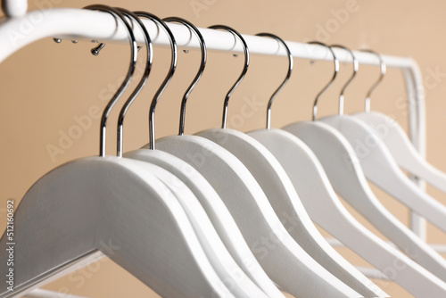 White clothes hangers on metal rack against beige background  closeup