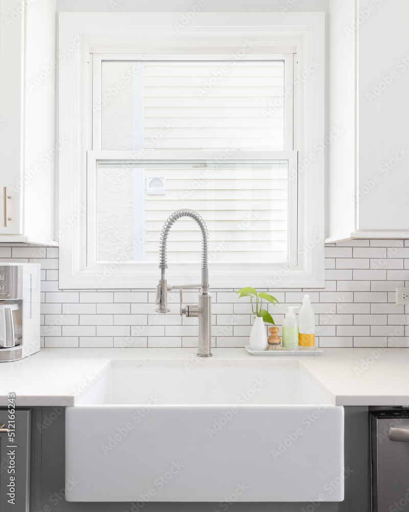 A kitchen sink detail shot with white and grey cabinets, a farmhouse sink, and white subway tile backsplash. A kitchen sink detail shot with white and grey cabinets, a farmhouse sink, and white subway tile backsplash.