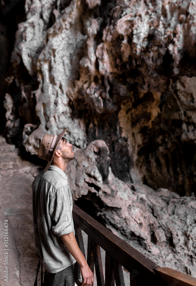 A young man wearing a hat is exploring a cave and having a look inside A young man wearing a hat is exploring a cave and having a look inside