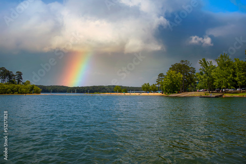 a gorgeous rainbow over Lake Allatoona with a beach and rippling blue lake water surrounded by lush green trees, grass and plants with clouds at Victoria Beach in Acworth Georgia USA photo