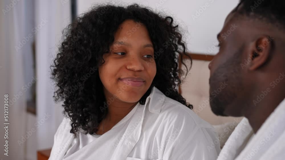 Smiling loving young woman looking at man talking with partner indoors. Portrait of happy confident relaxed African American wife enjoying leisure with husband at home in bedroom Smiling loving young woman looking at man talking with partner indoors. Portrait of happy confident relaxed African American wife enjoying leisure with husband at home in bedroom