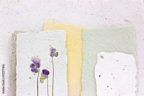 Dried viola flower pressed onto a sheet of handmade paper with a pronounced explicit texture. Reuse of materials.