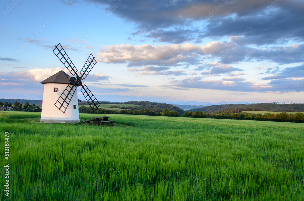 Windmill in the middle of a field with mountain views in the early summer evening