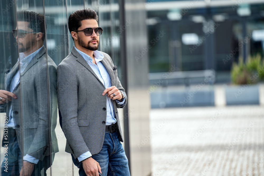 Outdoor photo of handsome elegant man wearing fashionable clothes and sunglasses, posing on the wall with reflections. City stale. Male model. Outdoor photo of handsome elegant man wearing fashionable clothes and sunglasses, posing on the wall with reflections. City stale. Male model.